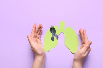 Female hands with grey ribbon and paper lungs on purple background