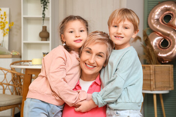 Little children and their grandmother hugging in kitchen. International Women's Day