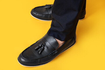 Legs of young man in black stylish shoes on yellow background