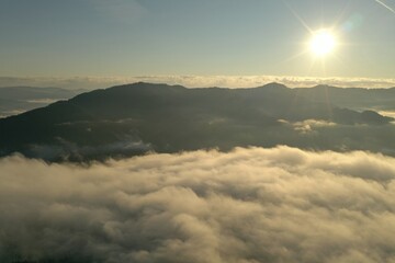Aerial view of beautiful mountains covered with fluffy clouds on sunny day