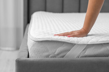 Woman touching new soft mattress on grey bed indoors, closeup