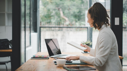 A focused businesswoman engages in multitasking at a well-organized home office space, exemplifying modern remote work.