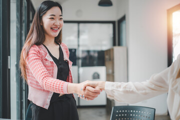 Two professional women with bright smiles engaging in a handshake in a modern office, symbolizing a...