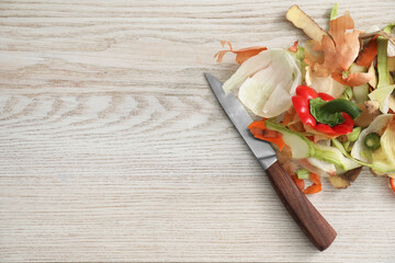 Peels of fresh vegetables and knife on white wooden table, flat lay. Space for text