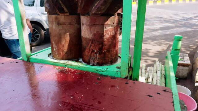 Traditional sugarcane juice extractor on a street cart with wood drums and crushed cane visible indian street food