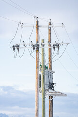 Wooden power poles standing tall against a blue sky with transformers and power lines in Rural...