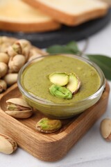 Tasty pistachio cream in bowl and nuts on light table, closeup