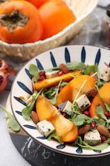 Tasty salad with persimmon, blue cheese, pomegranate and almonds served on white table, closeup