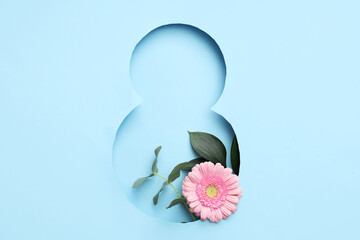 Cut paper in shape of figure 8 with beautiful gerbera flower and leaves on blue background. International Women's Day