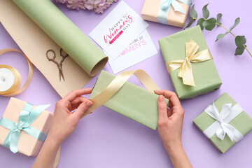 Female hands with gift boxes, cards and wrapping paper on purple background. International Women's...