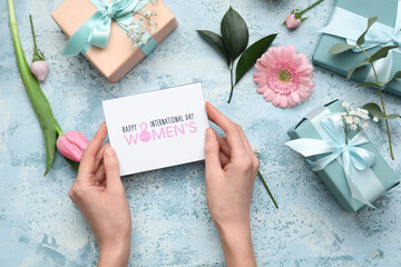 Female hands with gift card and boxes, beautiful flowers on blue background. International Women's...