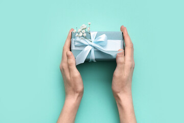 Female hands with gift box and gypsophila flowers on turquoise background. International Women's Day