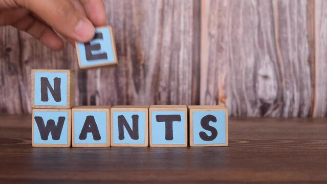 Prioritizing needs over wants concept. Human hand putting word needs on top of wants on wooden blocks.	