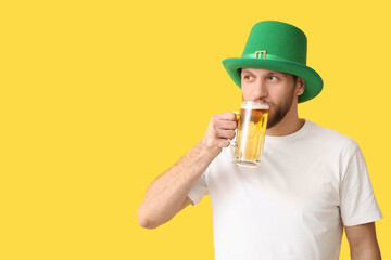 Young man in leprechaun hat drinking beer on yellow background. St. Patrick's Day celebration