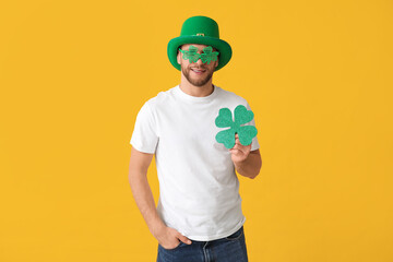 Young man in leprechaun hat and decorative glasses with clover on yellow background. St. Patrick's...