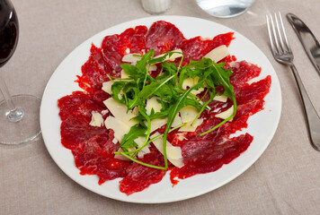 Carpaccio and cheese served on plate with arugula sprigs. Dish made of raw beef meat.