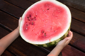 Kids hands holding half of watermelon on wooden table. Top view