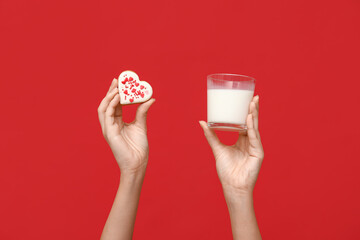 Woman with heart-shaped cookie and glass of milk on red background. Valentine's Day celebration