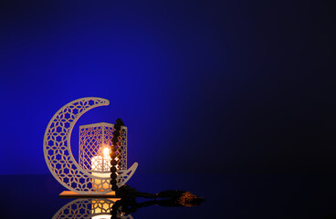 Decorative crescent with burning candle and prayer beads for Ramadan on dark blue background