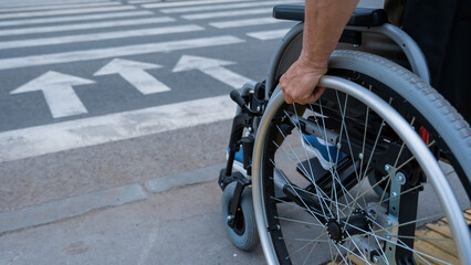 Rear view of an elderly woman in a wheelchair going to a pedestrian crossing. Close-up on wheels. 