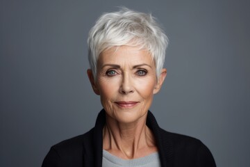 Portrait of a senior woman looking at camera against grey background. - obrazy, fototapety, plakaty