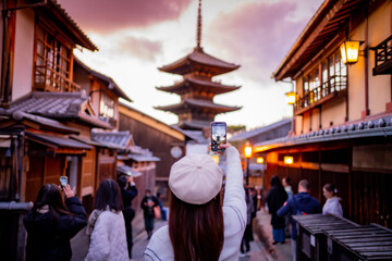 Yasaka Pagoda view and Hokan-ji Temple from Yasaka Dori street in Kyoto, Japan. Popular touristic street leading to Kyomizu Dera,Young female tourist taking photo with a mobile phone during sunset. - obrazy, fototapety, plakaty
