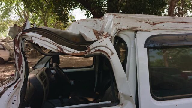Wrecked white van with severe roof and body damage parked under a tree depicting a traffic accident aftermath accidental car