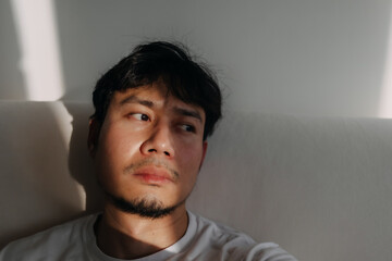 Close up face of lonely Asian man feeling depressed and bored in low light room.
