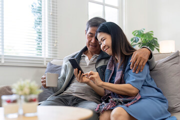 Portrait of Asian adorable senior couple using smartphone together video chatting with family in...