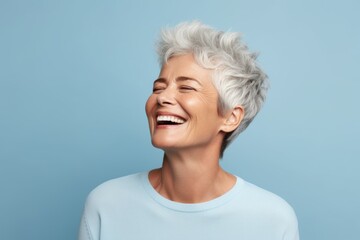 Happy senior woman with grey hair laughing and looking up on blue background