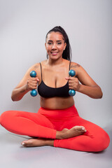 Beautiful, brunette, happy and smiling woman in gym clothes, sitting holding dumbbells. Healthy life.