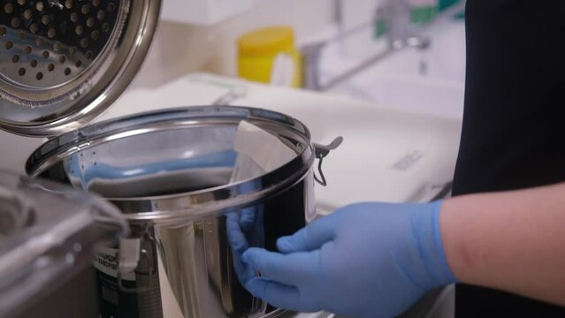 Laboratory female worker packing up medical instruments and putting into steam autoclave sterilization machine. Dental clinic. Disinfection process. Stomatology.