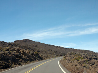 Driving to the Top of Haleakala volcano  on Maui Hawaii road with lifeless lava rock on roadsides on sunny day