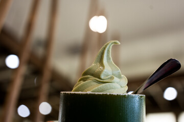 Green tea ice cream soft serve in a green cup and spoon on person hand. Ready to eat sweet food.