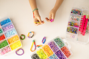 Girl makes rainbow bracelet from rubber bands crochet. Closeup of making decorative bracelet with elastic bands. Loom bracelets