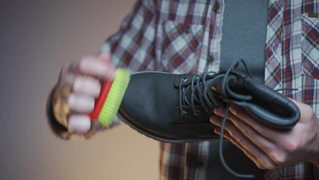 Topic care and brushing warm shoes expertly with small brush in workshop. Professional cleaning of nubuck shoes, suede autumn boots black, winter care and cleaning footwear. Boot maintenance studio. 