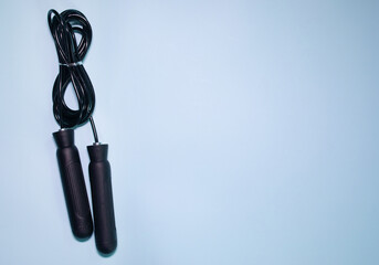 Black jump rope or skipping rope isolated on blue background. Sports, fitness, cardio, martial art and boxing accessories.