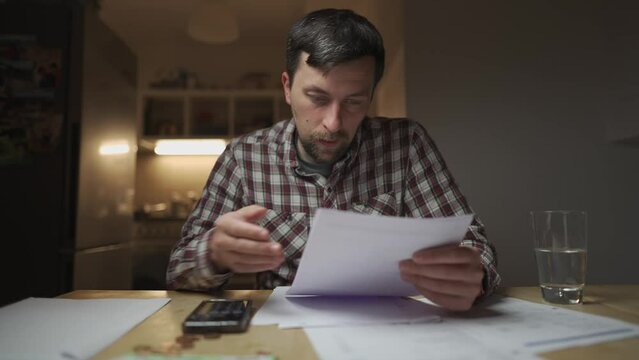 Financial problems. Sad man trying to find solution to taxes and debts at home in kitchen. Brainstorming ways of solving money troubles. Stressed male calculates costs, try to keep money in savings. 