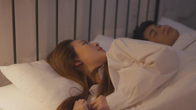 Asian woman secretly chatting to lover while lying in bed with husband. 