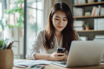 Business woman sitting at table using mobile smart phone during working on laptop computer at home office. Young Asian woman freelancer surfing the internet, online working from home