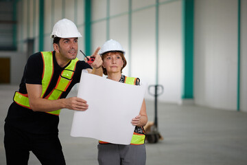 workers or engineers planning from work on blueprint drawing paper and pointing to something in the factory