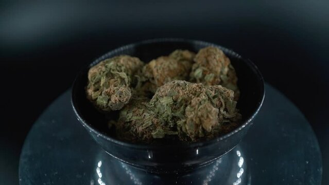 Dreamy Green Dried Marijuana Buds Close Up Shot, pile of dried marijuana plants in a shiny bowl, trichomes strains, on a reflecting rotating stand, studio lights, cinematic crane rotating slow motion