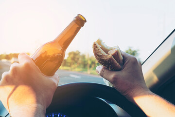 Man eating hotdog with beer while driving a car dangerously - obrazy, fototapety, plakaty