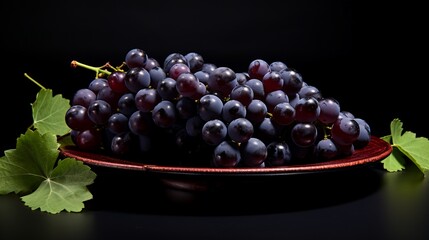 Black grapes on a plate on a black background. Studio shot.