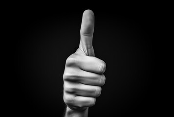 Man's hand shows thumbs up on a black background - obrazy, fototapety, plakaty