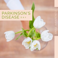 Composition of parkinson's disease day text over woman holding bunch of white tulips