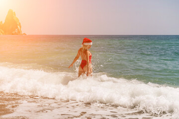 A woman in Santa hat on the seashore, dressed in a red swimsuit. New Year's celebration in a hot country