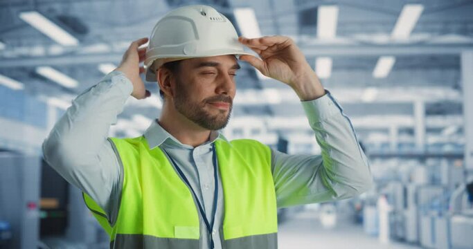 Portrait of Successful Caucasian Male Engineer Putting On a White Hard Hat at Electronics Manufacturing Factory. Heavy Industry Specialist Thinking About Advanced Technology Projects On Production.