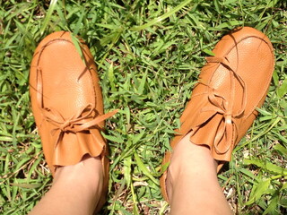 woman wearing the artificial brown leather shoes, standing on the natural green grass lawn in daylight