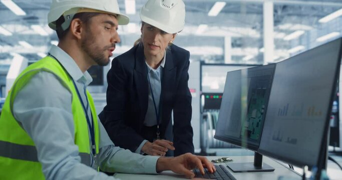 Caucasian Female Manager And Male Industrial Engineer Using Desktop Computer With Microchip Prototype at Automated Electronics Factory. Diverse Colleagues Discussing Production Of High-Tech Devices.